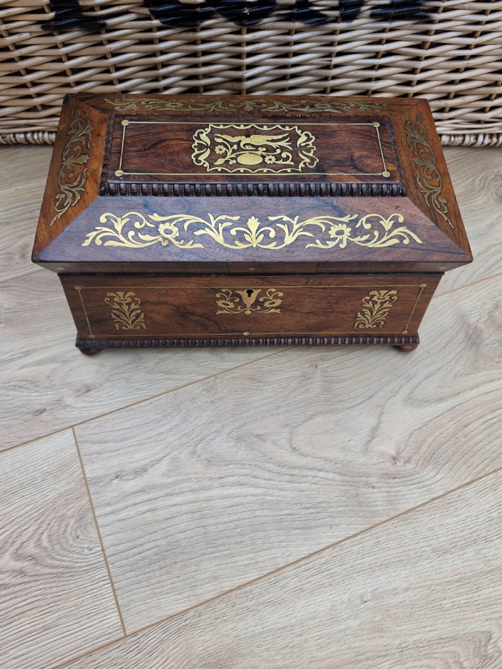 A Regency period dark rosewood tea caddy featuring ornate brass floral scrollwork inlay, gadrooned borders, and a central bird motif on the hinged lid.