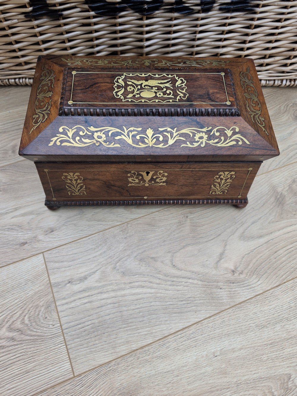 A Regency period dark rosewood tea caddy featuring ornate brass floral scrollwork inlay, gadrooned borders, and a central bird motif on the hinged lid. View VI