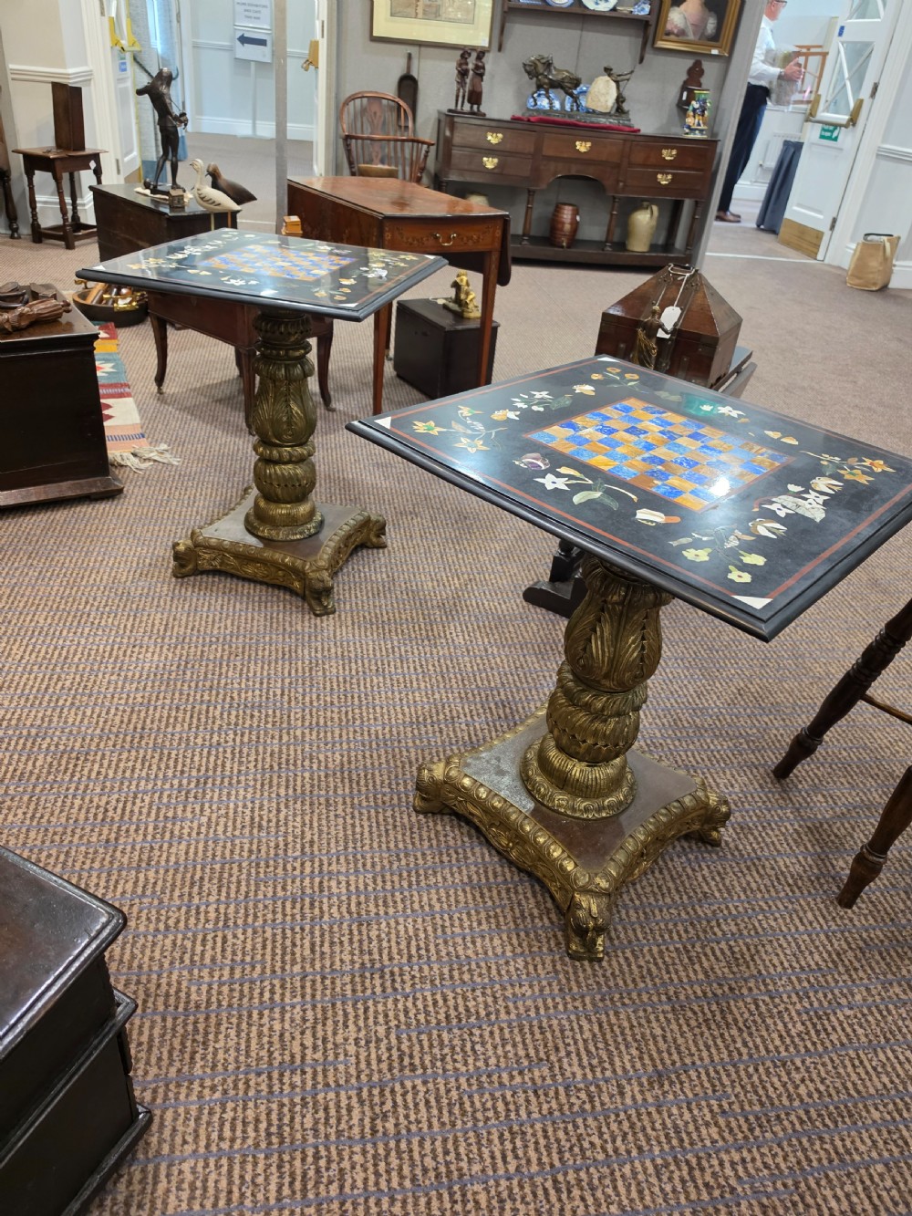 A pair of 19th-century occasional tables featuring square black marble tops inlaid with colourful pietra dura chessboard patterns and floral borders on carved giltwood pedestal bases.