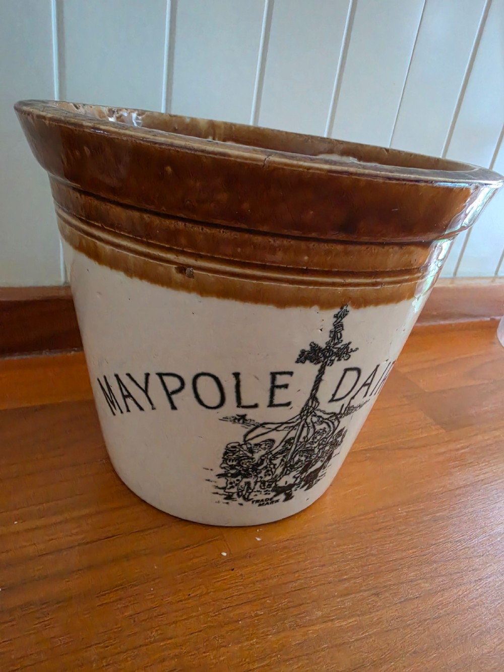 A Victorian cream stoneware dairy crock featuring a brown glazed rim and black transfer-printed Maypole Dairy lettering and illustration.