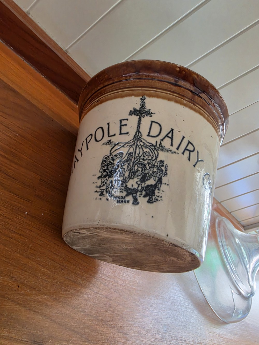A Victorian cream stoneware dairy crock featuring a brown glazed rim and black transfer-printed Maypole Dairy lettering and illustration. View IV