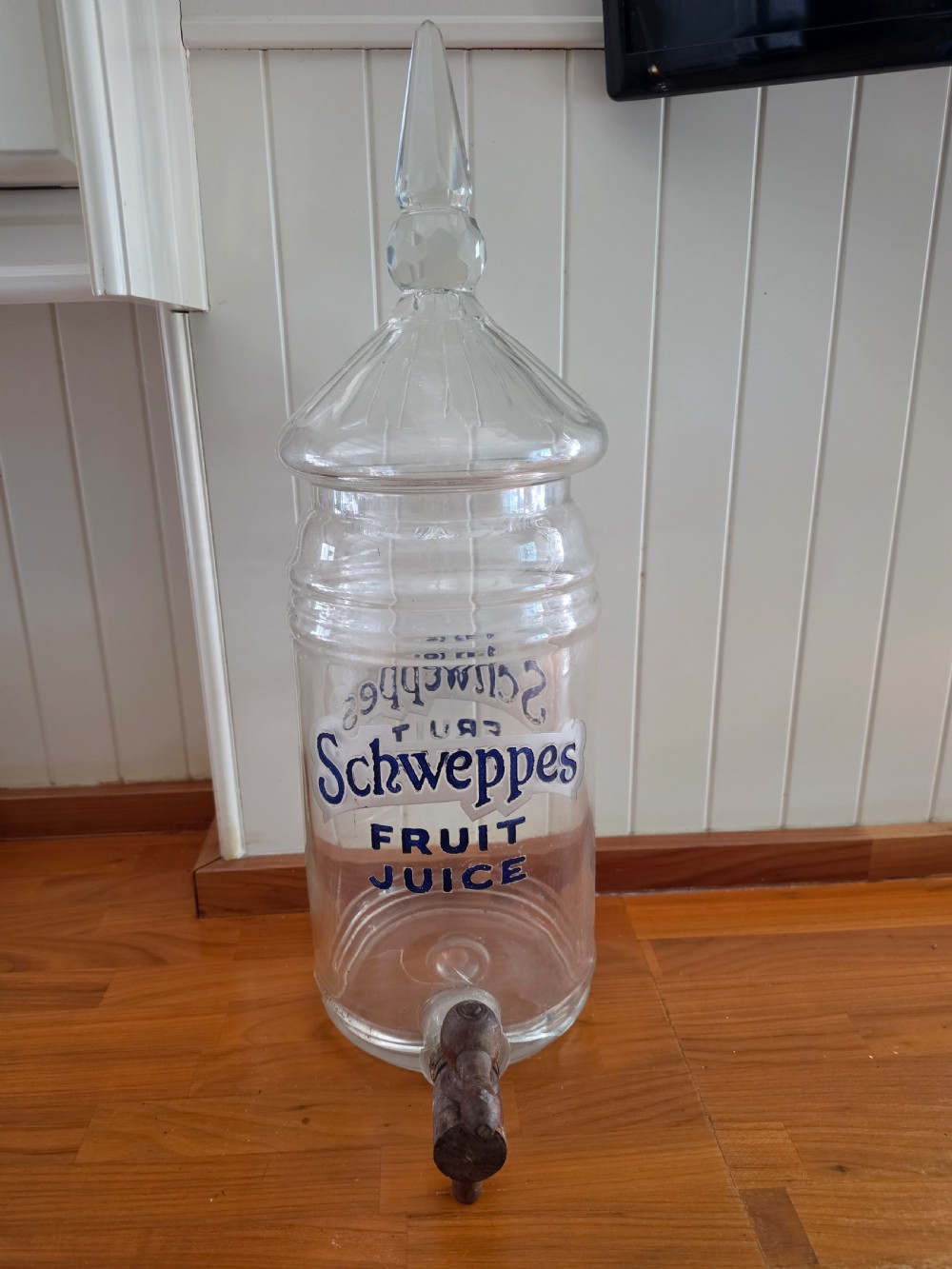 A large clear glass Schweppes fruit juice dispenser featuring printed lettering, a pointed finial lid, and a metal tap at the base.