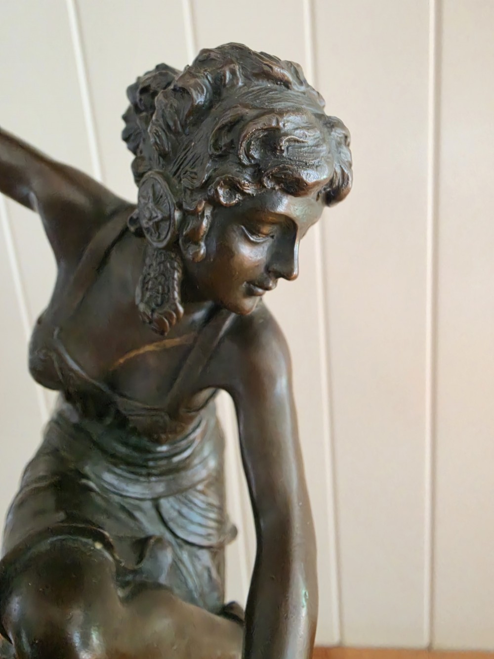 A dark patinated bronze figure depicting a female dancer in mid-motion with raised arms, standing balanced on a circular base. View II