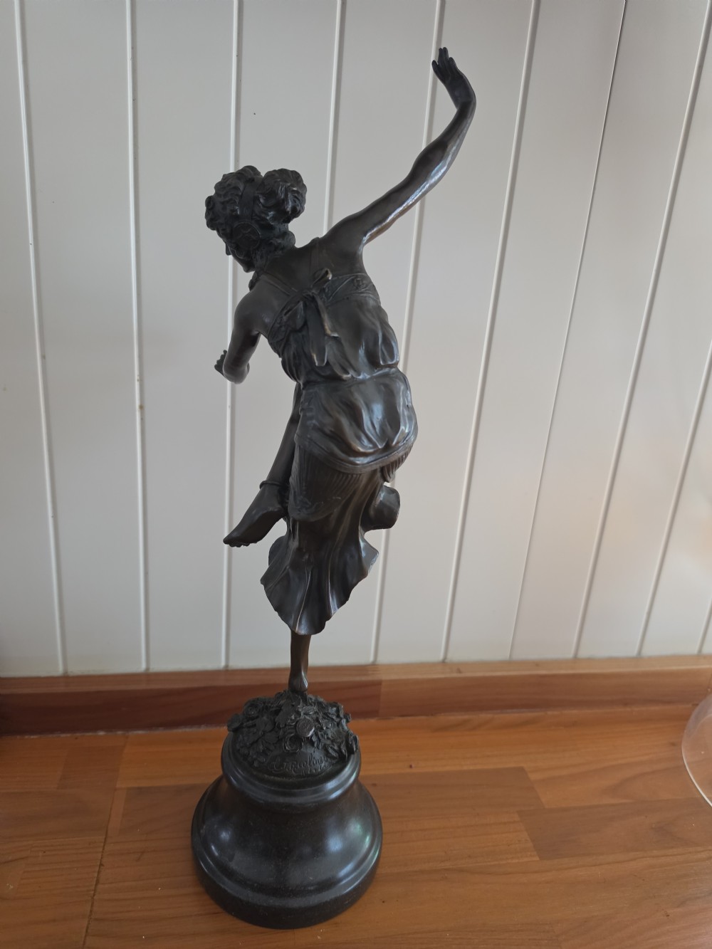A dark patinated bronze figure depicting a female dancer in mid-motion with raised arms, standing balanced on a circular base. View IV