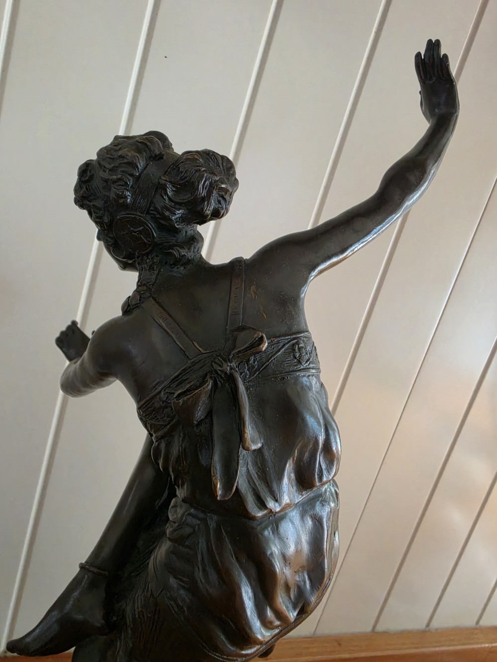 A dark patinated bronze figure depicting a female dancer in mid-motion with raised arms, standing balanced on a circular base. View VI