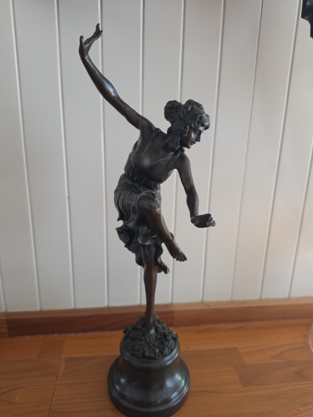 A dark patinated bronze figure depicting a female dancer in mid-motion with raised arms, standing balanced on a circular base. View VII