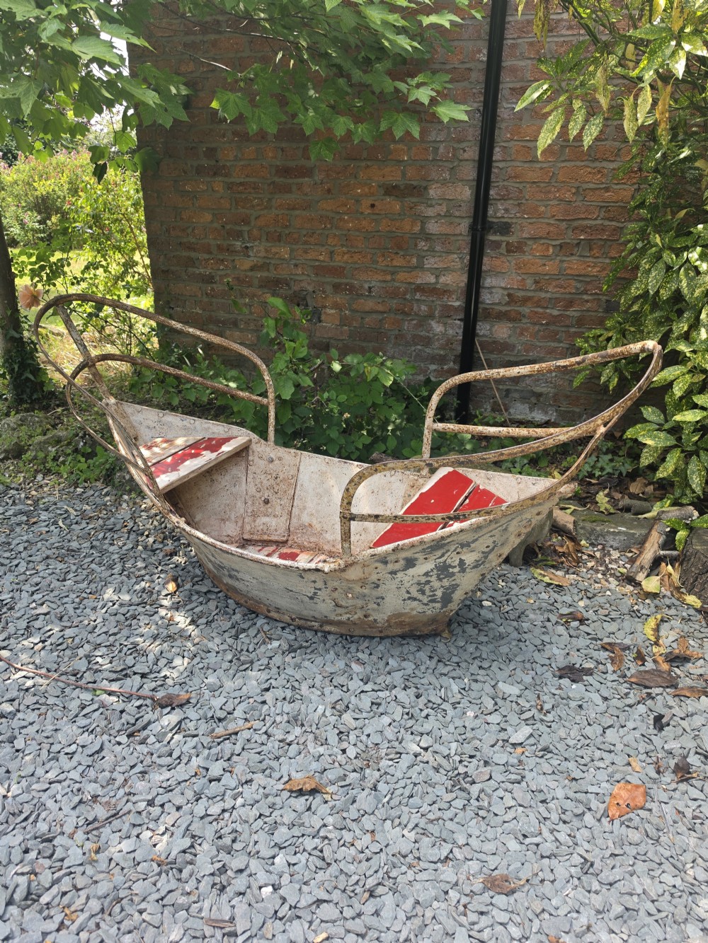 A late nineteenth-century riveted metal boat fairground ride with curved tubular iron safety railings and weathered cream and red painted panels. View II