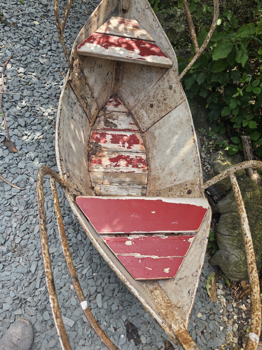 A late nineteenth-century riveted metal boat fairground ride with curved tubular iron safety railings and weathered cream and red painted panels. View III