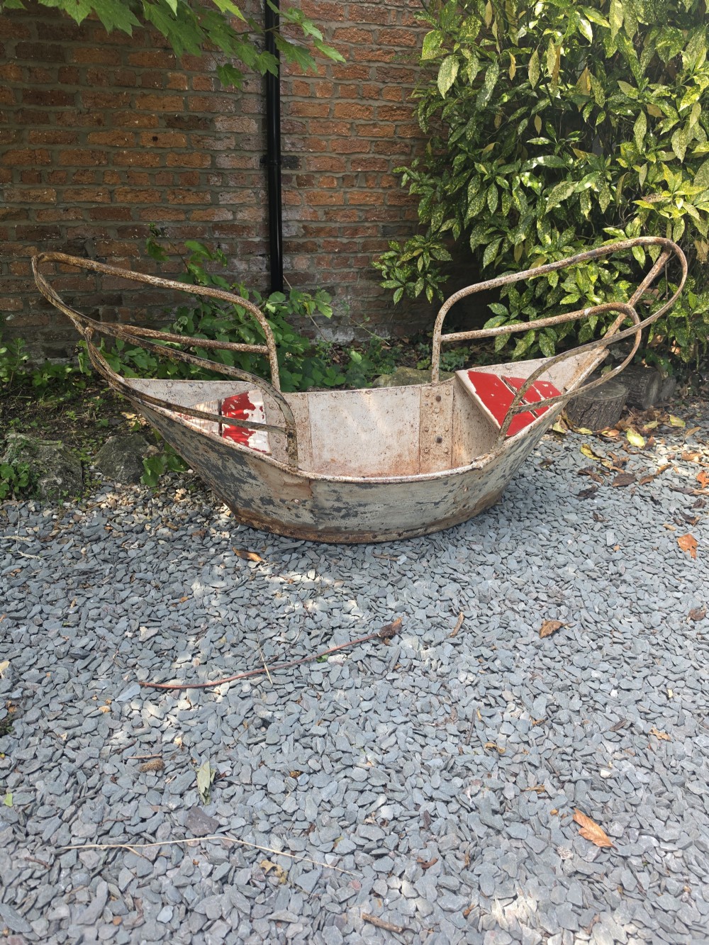 A late nineteenth-century riveted metal boat fairground ride with curved tubular iron safety railings and weathered cream and red painted panels. View IV