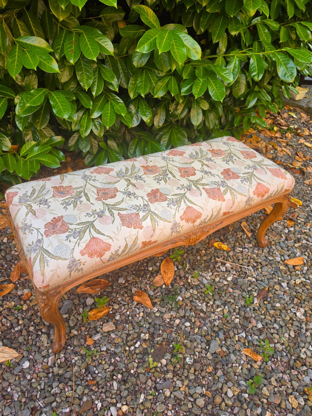 A long 19th-century stool crafted from carved walnut with cabriole legs and upholstered in a floral pattern fabric.
