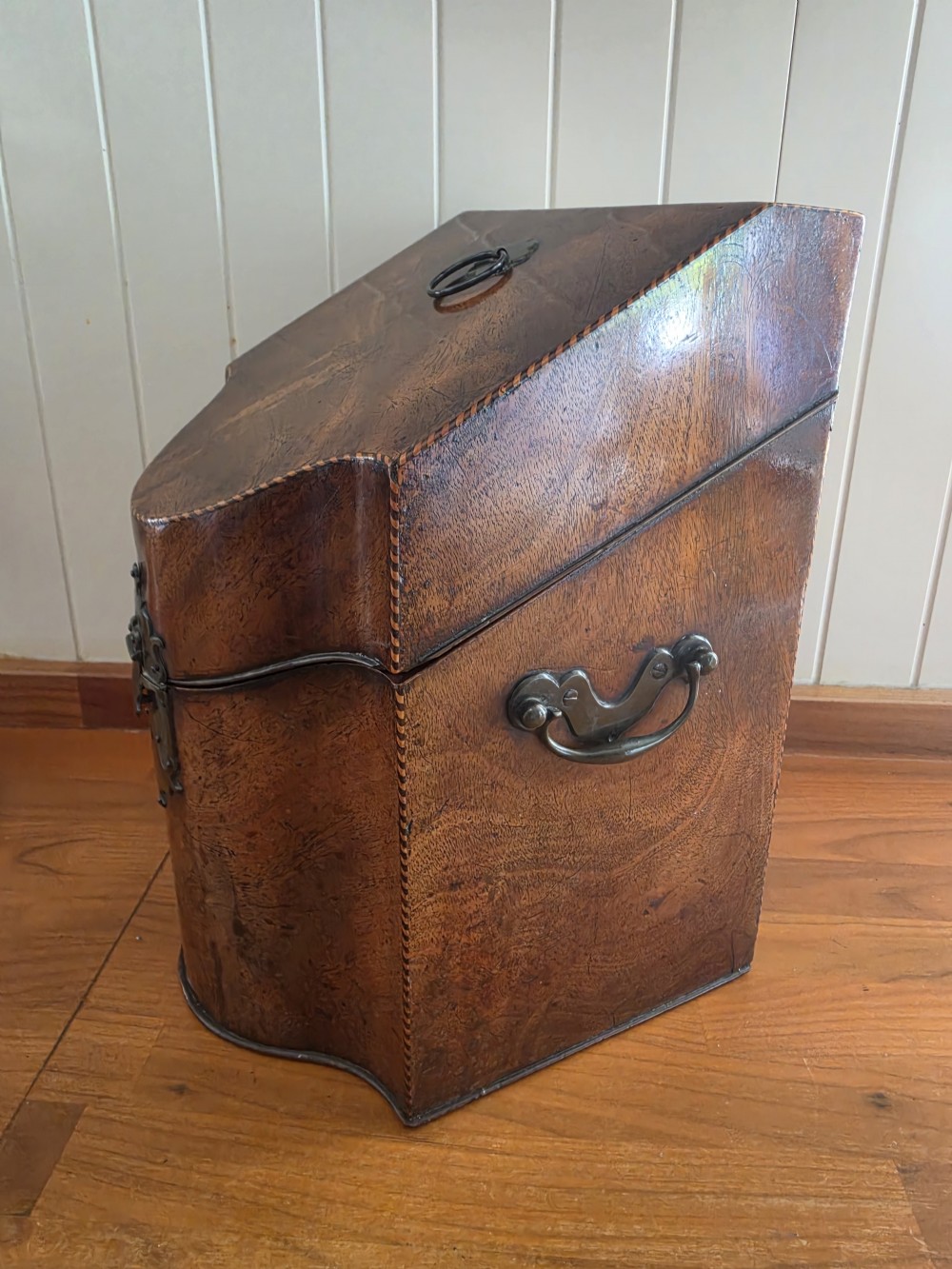 A Georgian mahogany knife box featuring a sloped lid, serpentine front, brass lock plate, ring handle, and edge stringing. View III