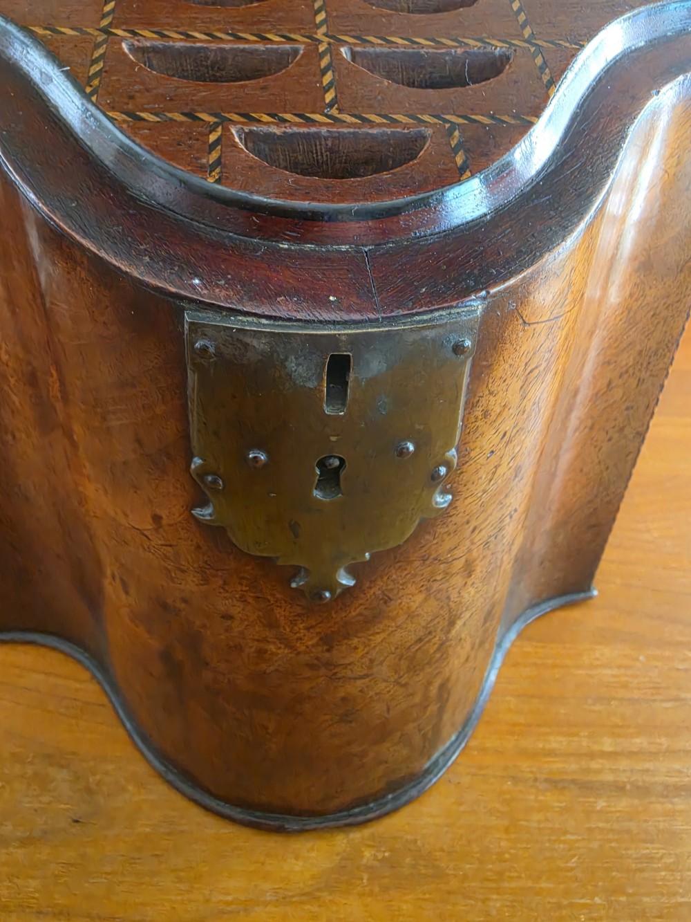 A Georgian mahogany knife box featuring a sloped lid, serpentine front, brass lock plate, ring handle, and edge stringing. View IV