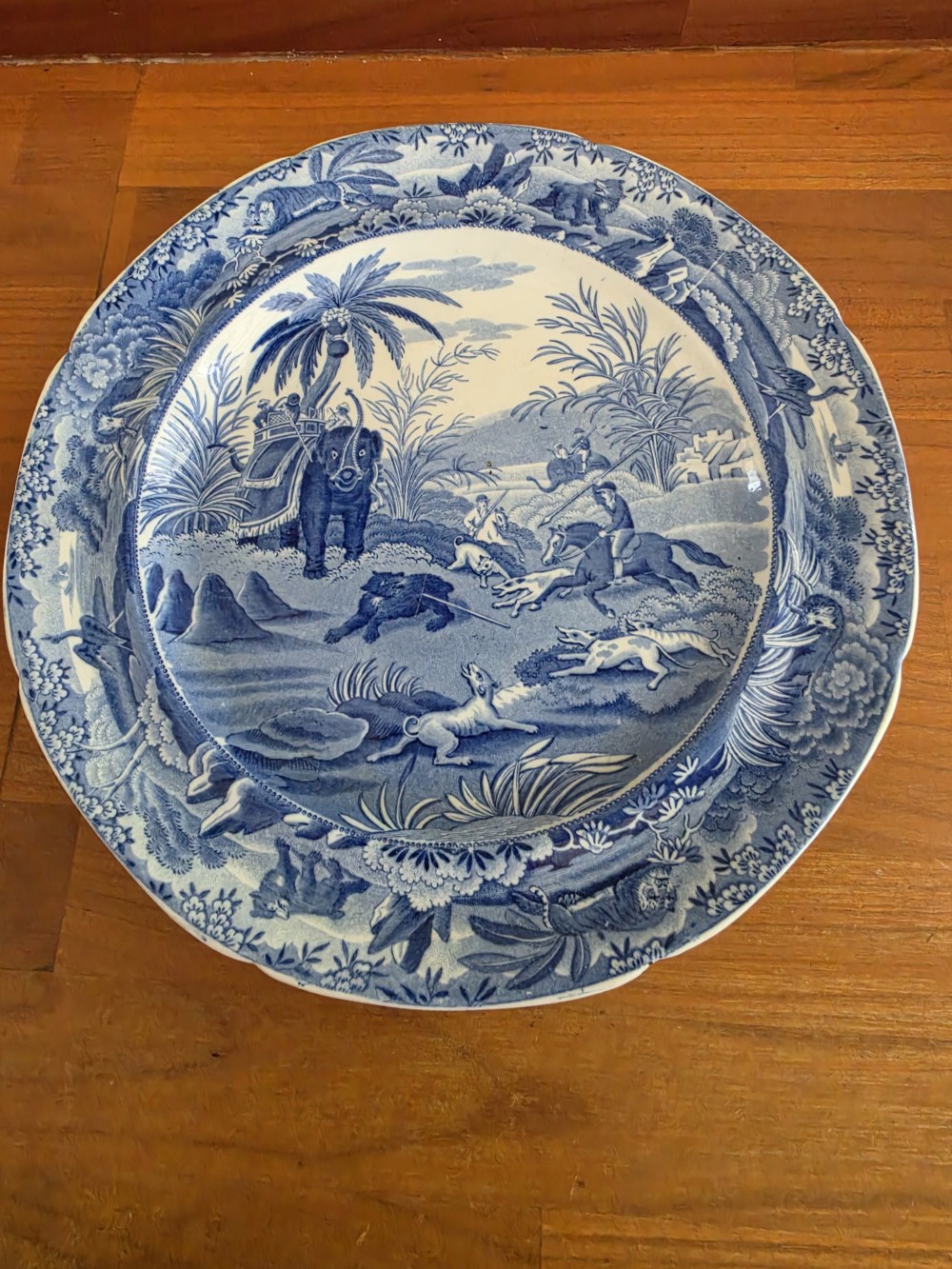 A circular blue and white ceramic transferware plate depicting a classical Indian hunting scene with horses, hounds, an elephant, and a bear. View V