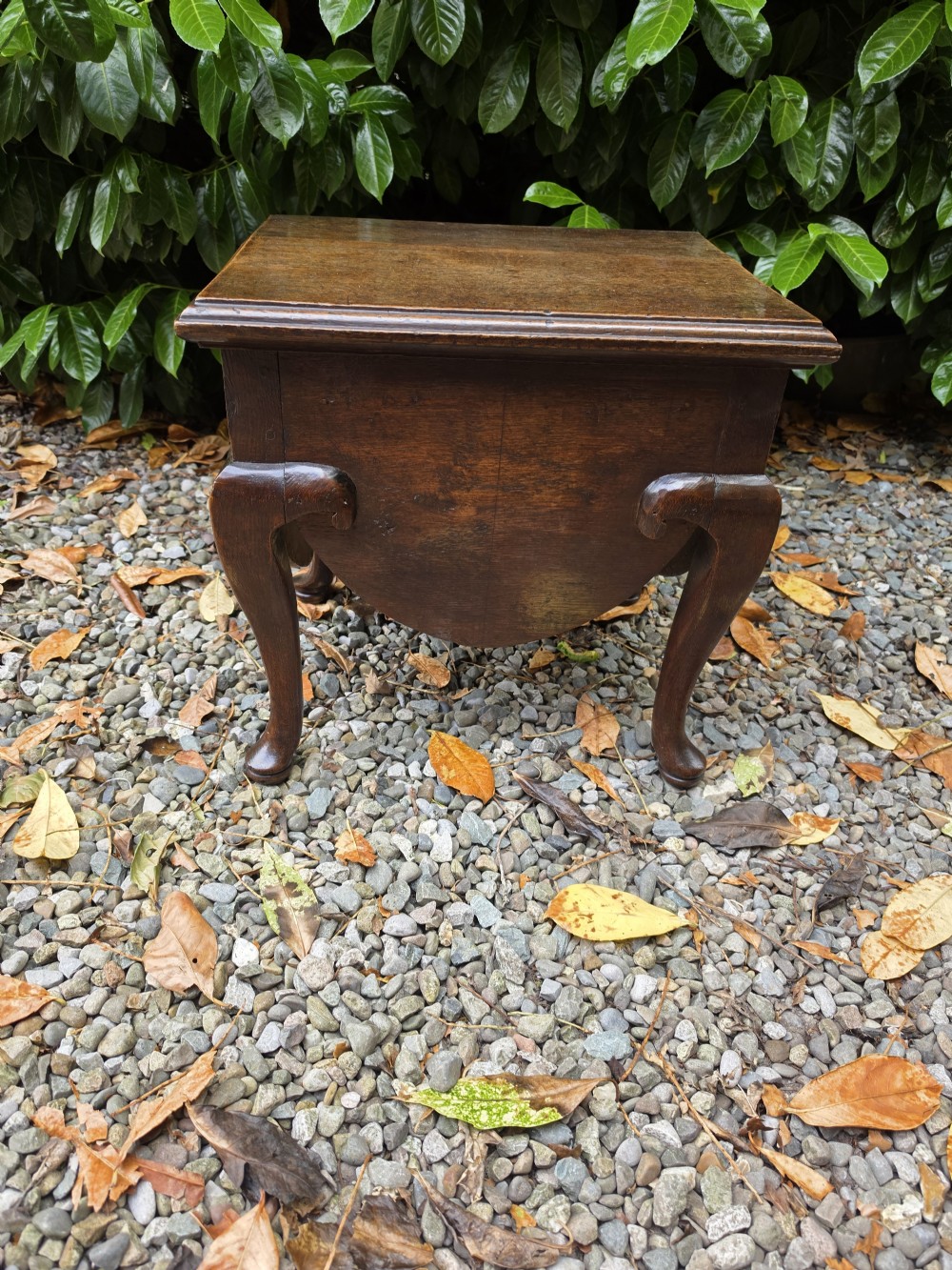 An early eighteenth-century dark oak stool featuring a solid rectangular top with molded edges, a deeply curved apron, and four cabriole legs with pad feet.