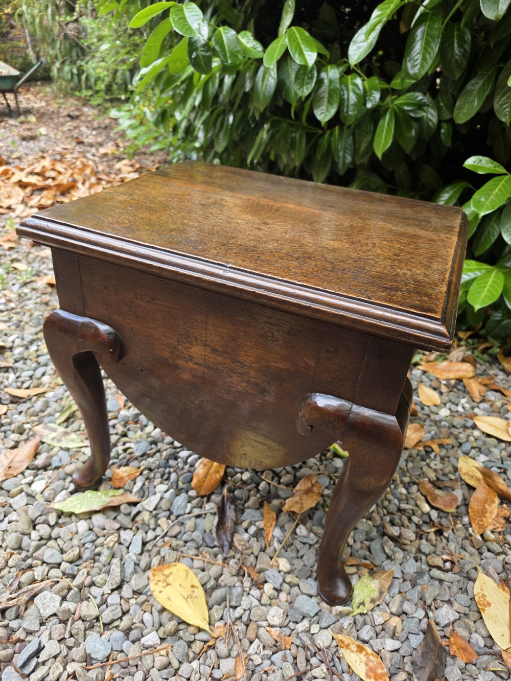 An early eighteenth-century dark oak stool featuring a solid rectangular top with molded edges, a deeply curved apron, and four cabriole legs with pad feet. View III