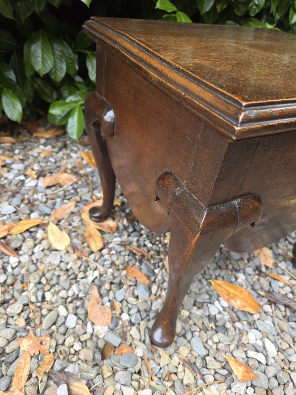 An early eighteenth-century dark oak stool featuring a solid rectangular top with molded edges, a deeply curved apron, and four cabriole legs with pad feet. View IV