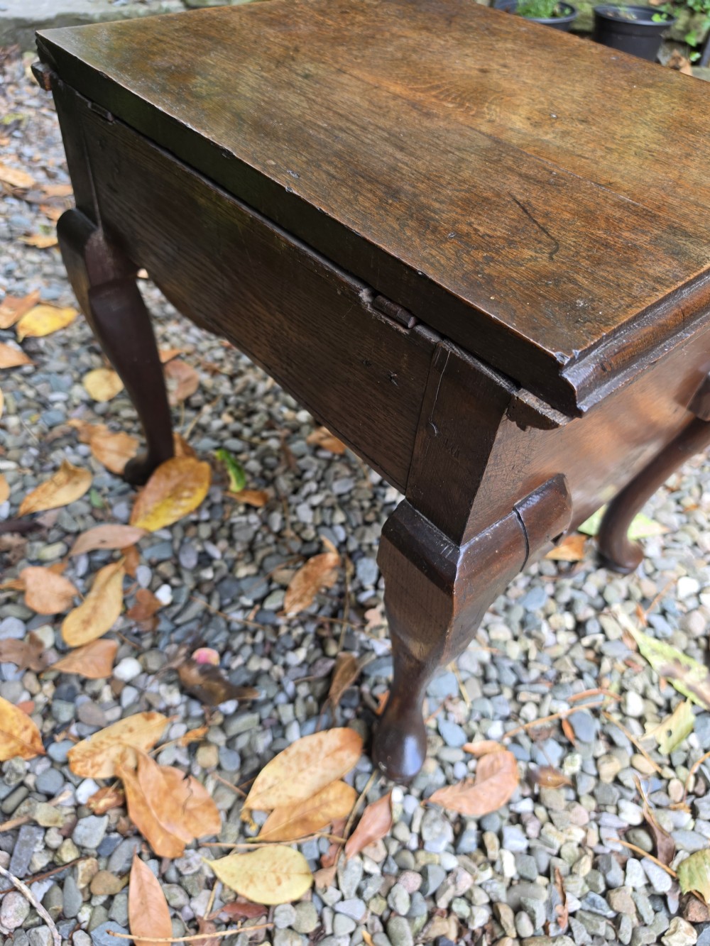 An early eighteenth-century dark oak stool featuring a solid rectangular top with molded edges, a deeply curved apron, and four cabriole legs with pad feet. View V