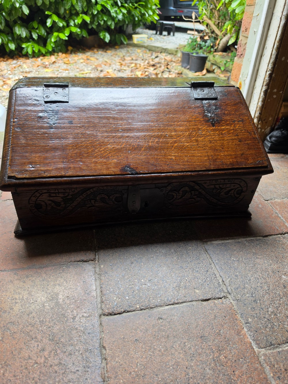 A late seventeenth-century dark oak slant-front Bible box featuring hand-carved scrollwork on the front panel and dark iron strap hinges. View II