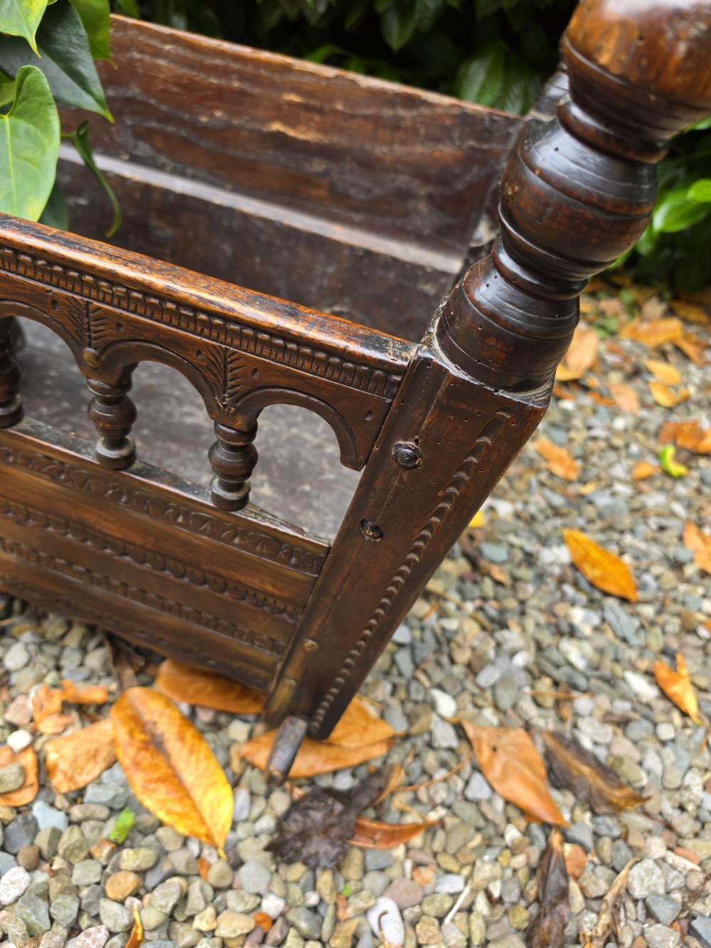 A 17th-century carved dark oak and fruitwood rocking cradle featuring turned corner finials and a spindle gallery side rail. View III