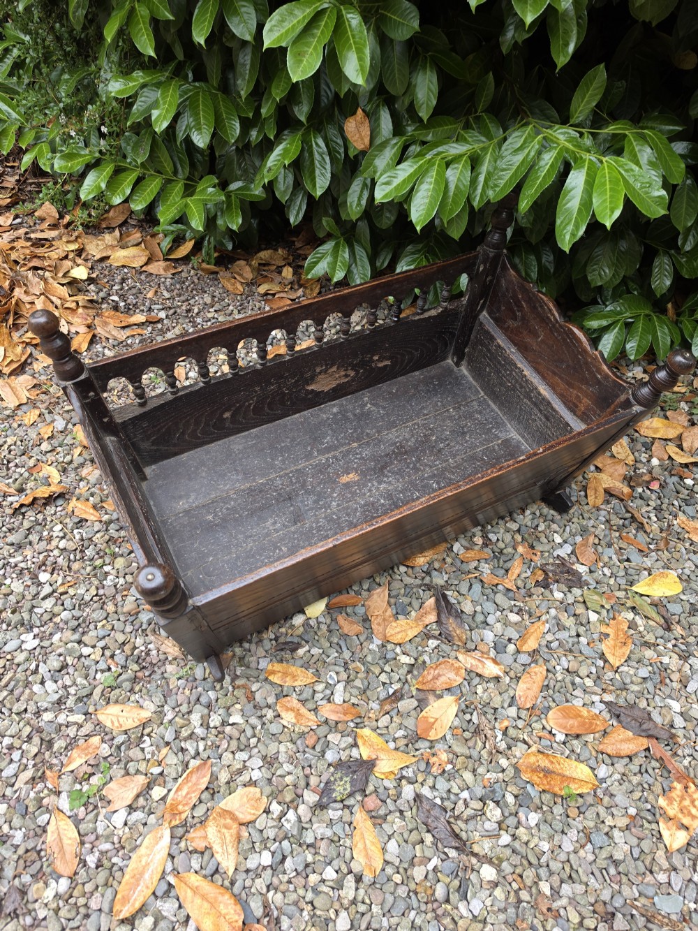 A 17th-century carved dark oak and fruitwood rocking cradle featuring turned corner finials and a spindle gallery side rail. View V