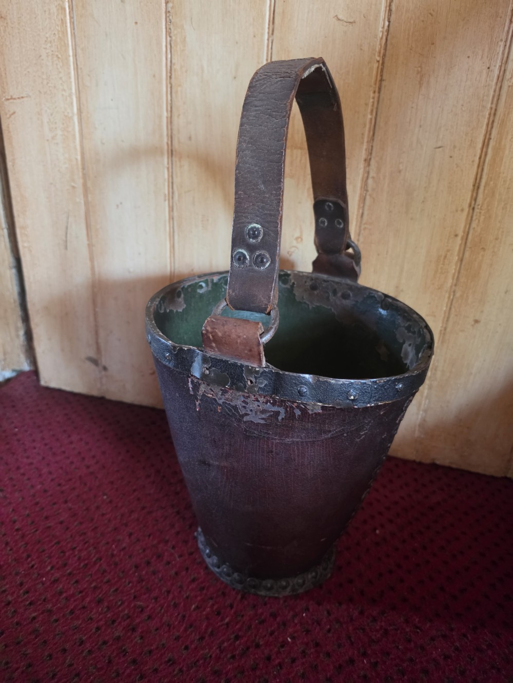 A conical dark brown leather fire bucket with metal studding along the rim and side seams and an attached leather handle. View IV