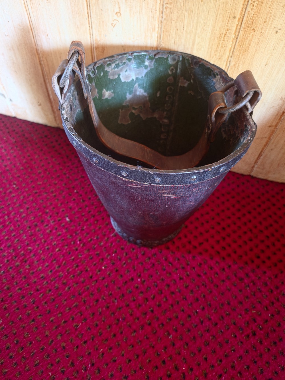 A conical dark brown leather fire bucket with metal studding along the rim and side seams and an attached leather handle. View V