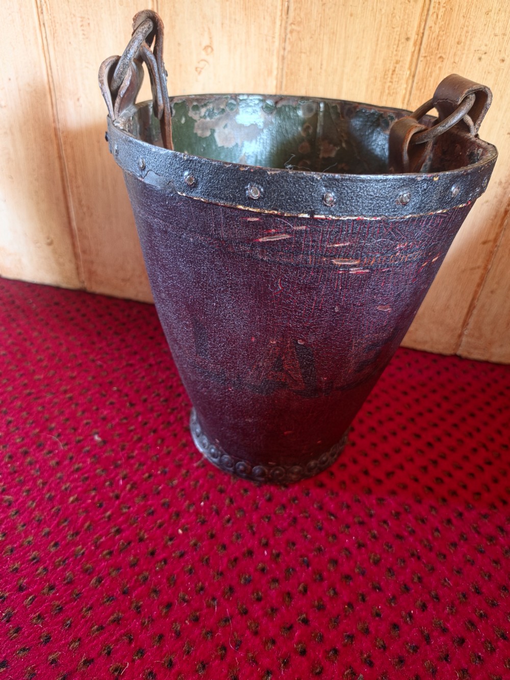 A conical dark brown leather fire bucket with metal studding along the rim and side seams and an attached leather handle. View VI