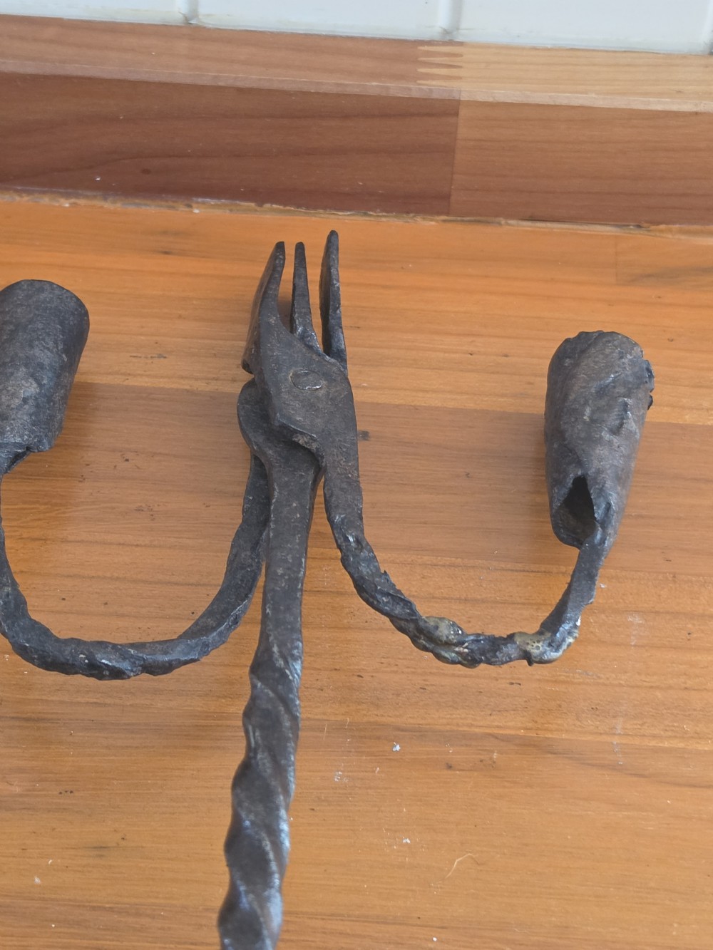 A hand-forged wrought iron rushlight holder featuring a central spring nip clamp, two candle sockets on curved side arms, a twisted stem, and a hoop base. View II