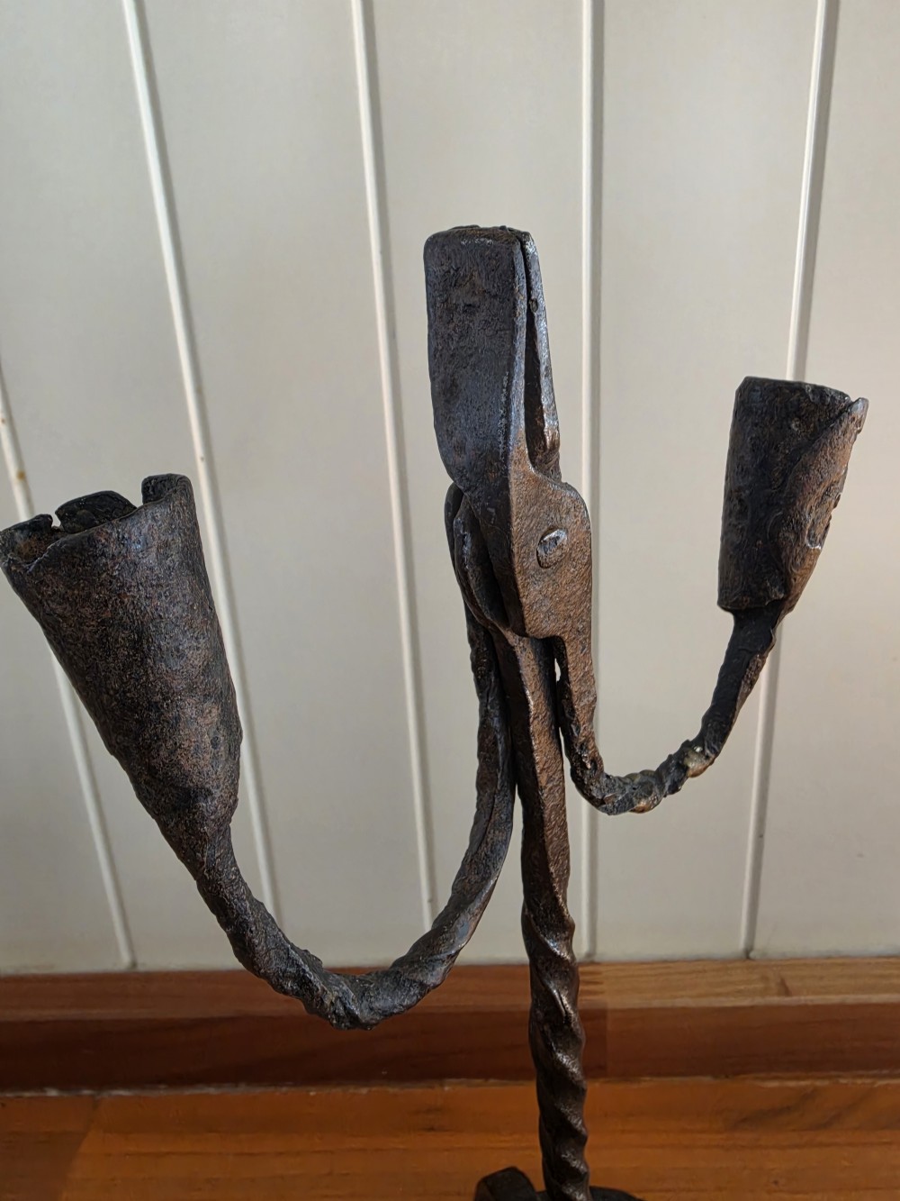 A hand-forged wrought iron rushlight holder featuring a central spring nip clamp, two candle sockets on curved side arms, a twisted stem, and a hoop base. View IV
