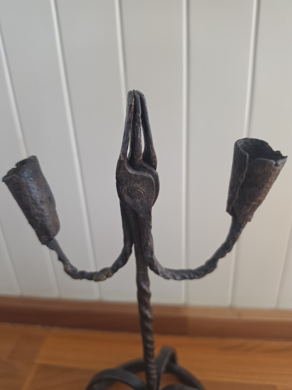 A hand-forged wrought iron rushlight holder featuring a central spring nip clamp, two candle sockets on curved side arms, a twisted stem, and a hoop base. View V