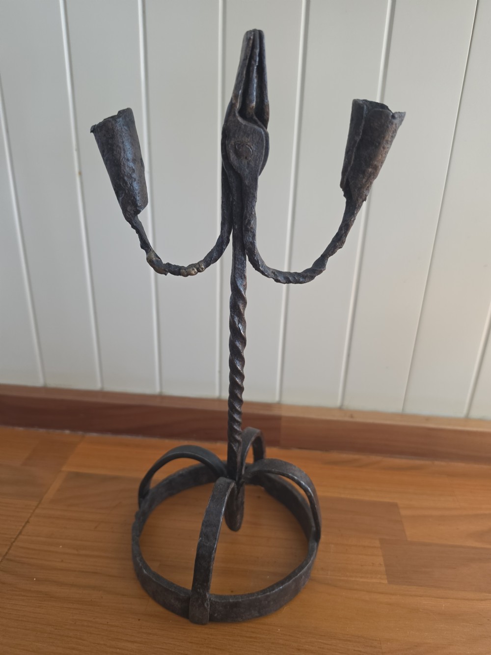 A hand-forged wrought iron rushlight holder featuring a central spring nip clamp, two candle sockets on curved side arms, a twisted stem, and a hoop base. View VI