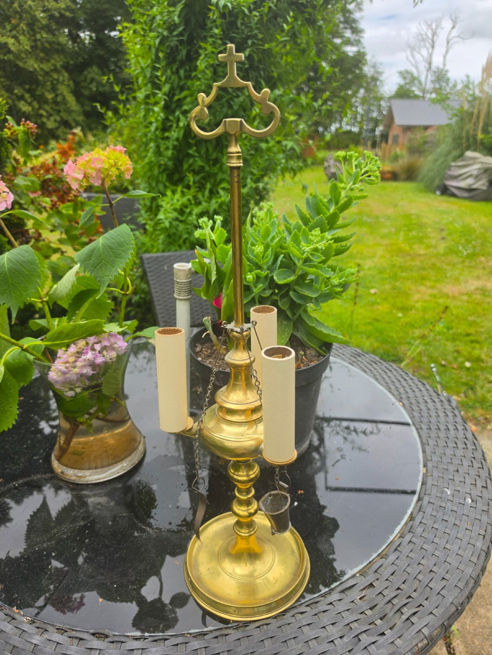 A 19th-century brass student lamp with a circular stepped base, central turned stem with loop handle, three candle sleeves, and miniature brass tools suspended from chains.