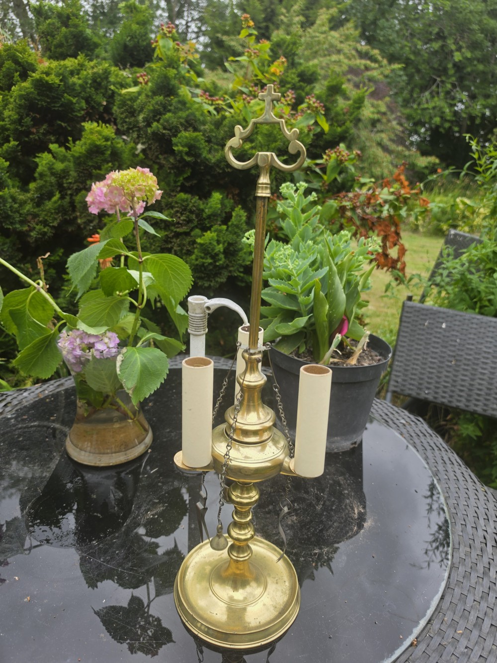 A 19th-century brass student lamp with a circular stepped base, central turned stem with loop handle, three candle sleeves, and miniature brass tools suspended from chains. View V