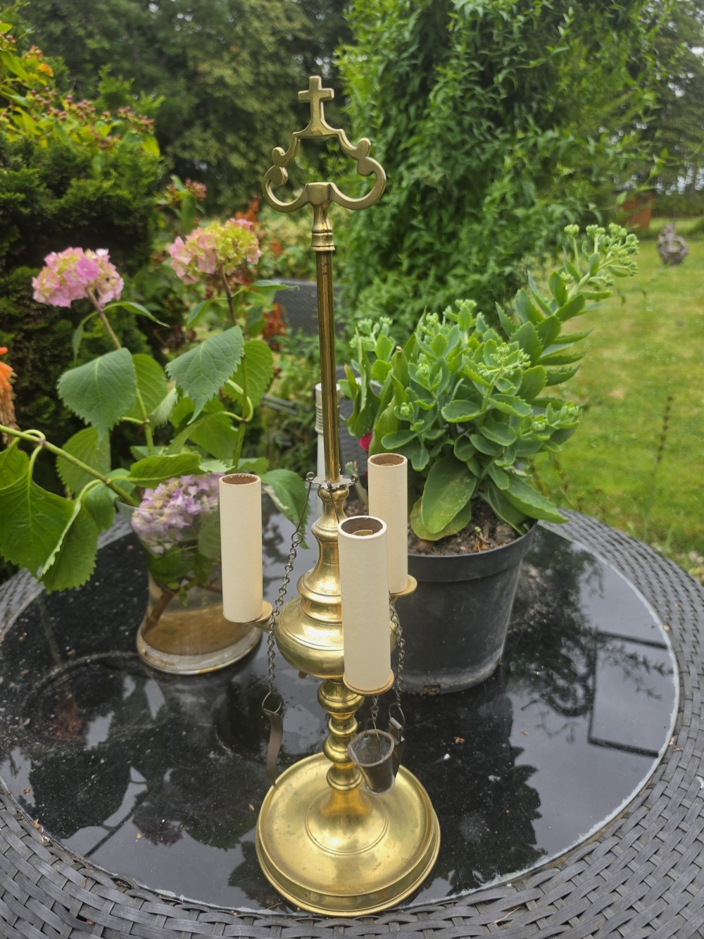 A 19th-century brass student lamp with a circular stepped base, central turned stem with loop handle, three candle sleeves, and miniature brass tools suspended from chains. View VI