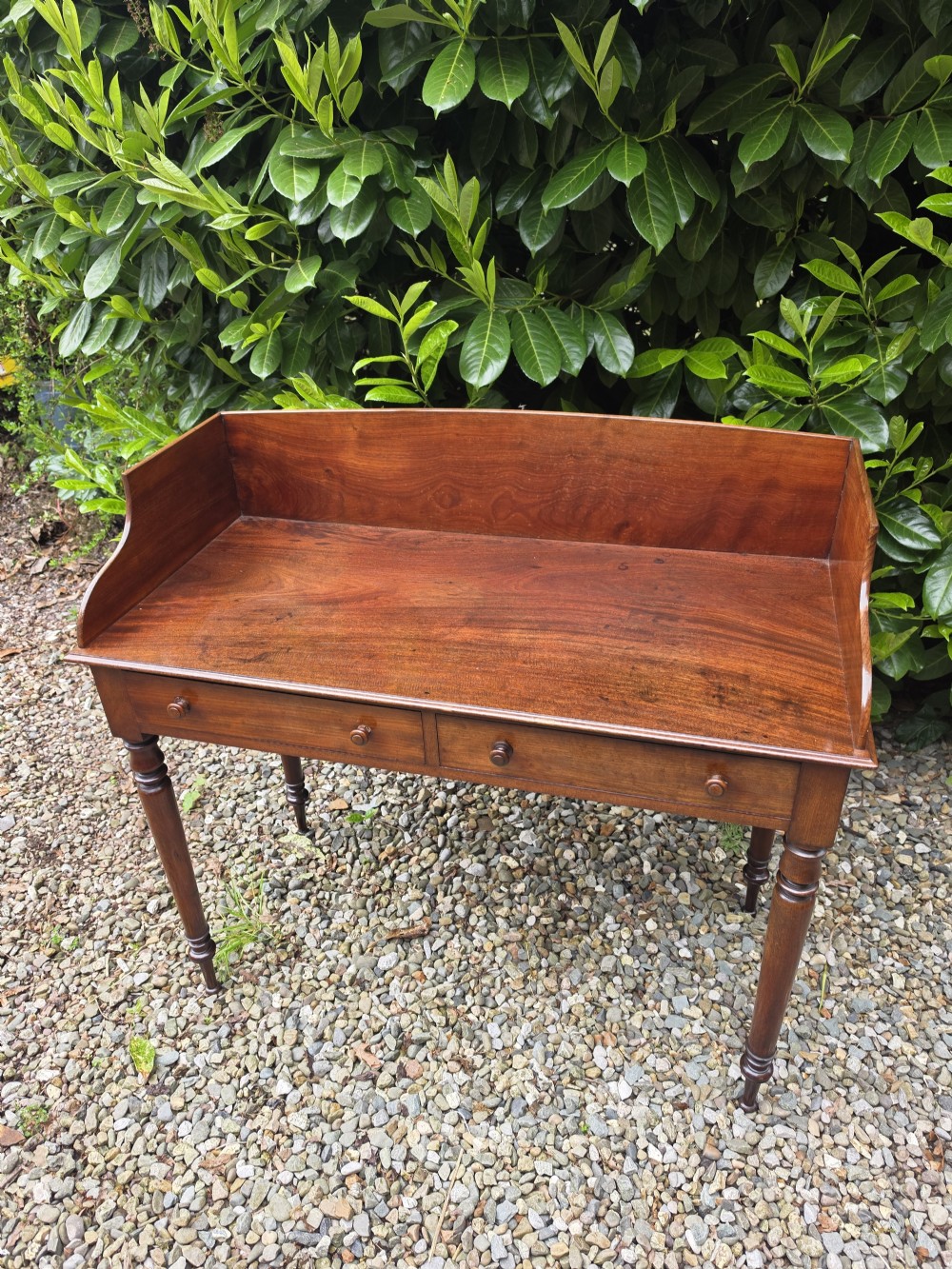 An antique Georgian mahogany side table featuring two drawers with turned wooden knobs, four turned legs, and a high curved gallery back. View II