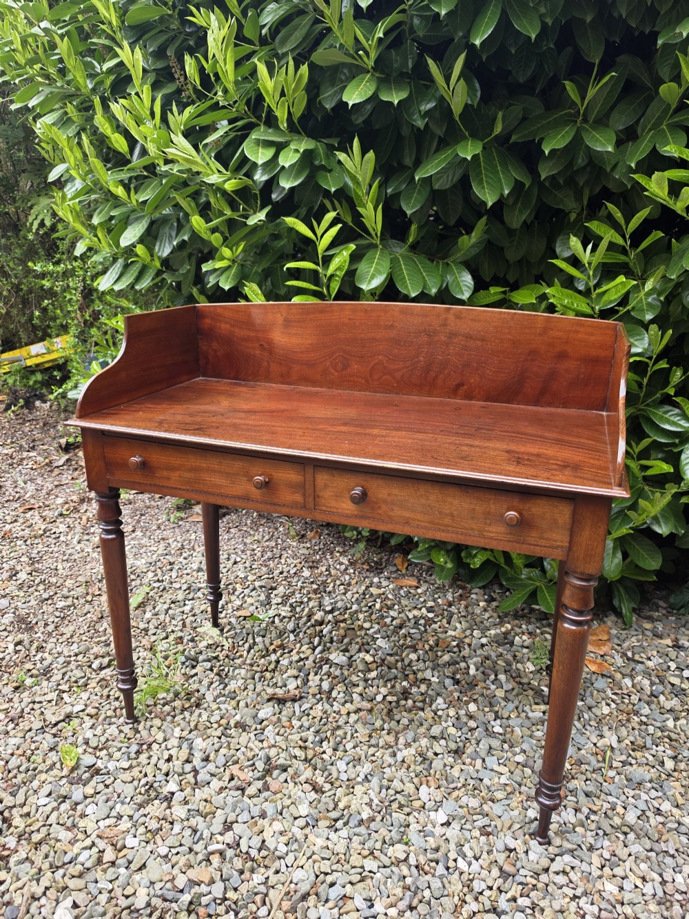 An antique Georgian mahogany side table featuring two drawers with turned wooden knobs, four turned legs, and a high curved gallery back. View VIII