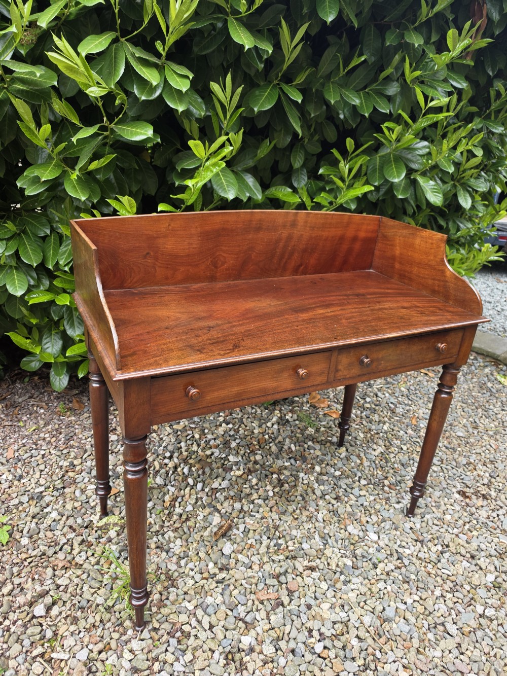 An antique Georgian mahogany side table featuring two drawers with turned wooden knobs, four turned legs, and a high curved gallery back. View IX