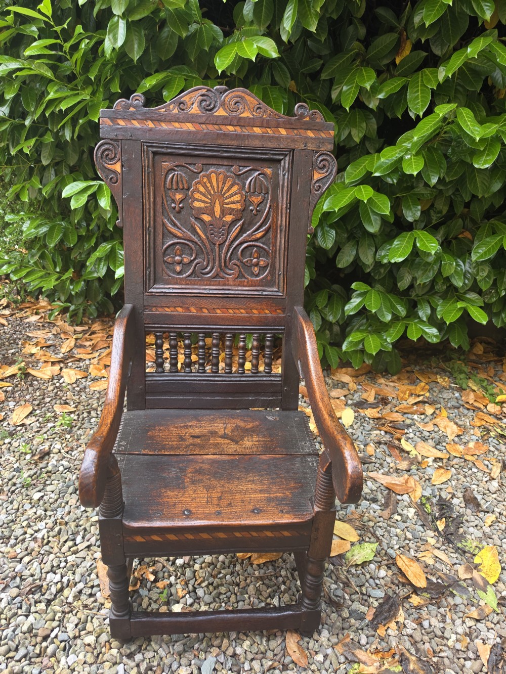 A 17th-century dark oak wainscot armchair featuring a carved back panel with floral inlay, turned front legs, scrolled cresting, and wooden peg joinery. View II