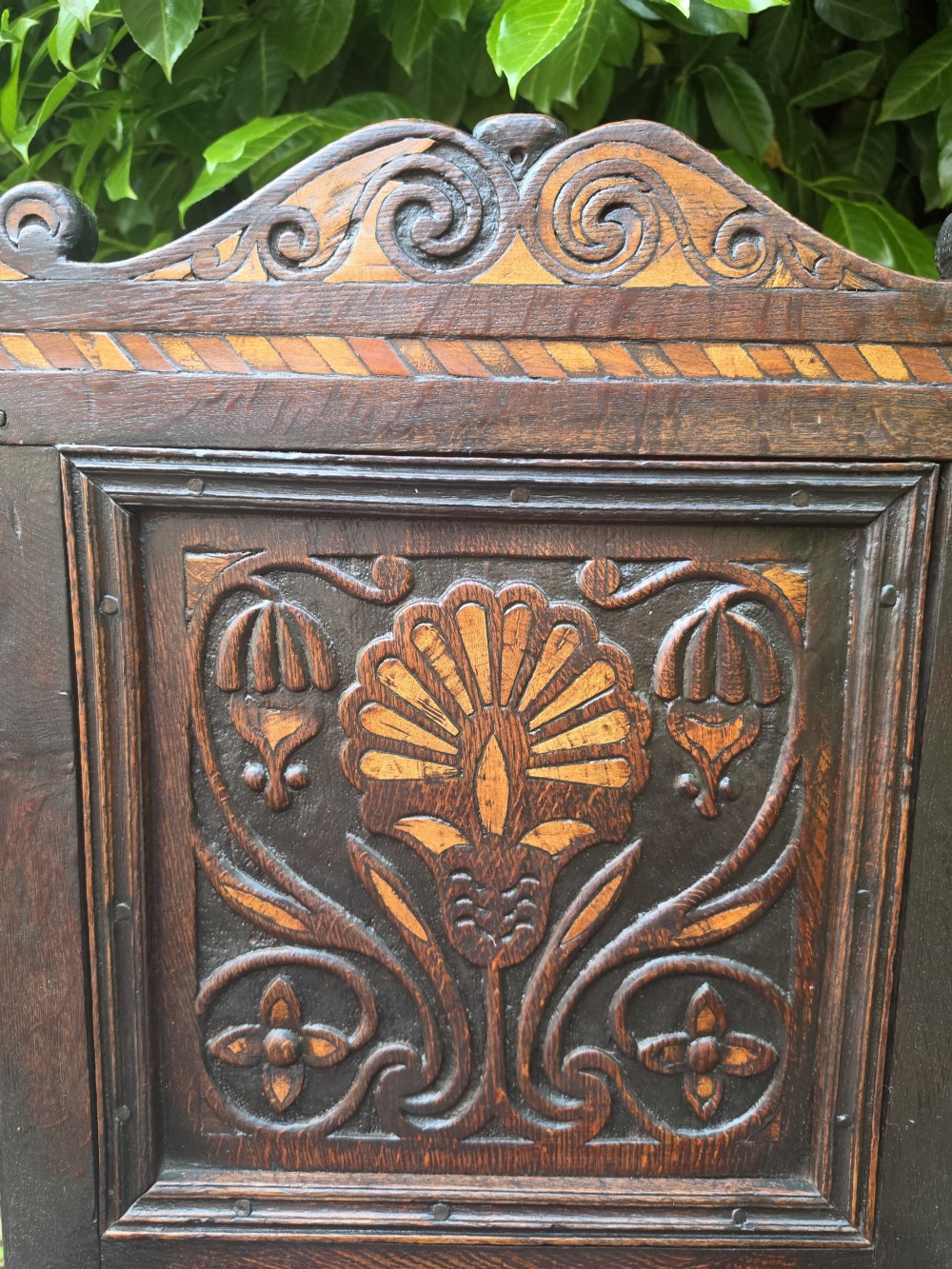 A 17th-century dark oak wainscot armchair featuring a carved back panel with floral inlay, turned front legs, scrolled cresting, and wooden peg joinery. View IV
