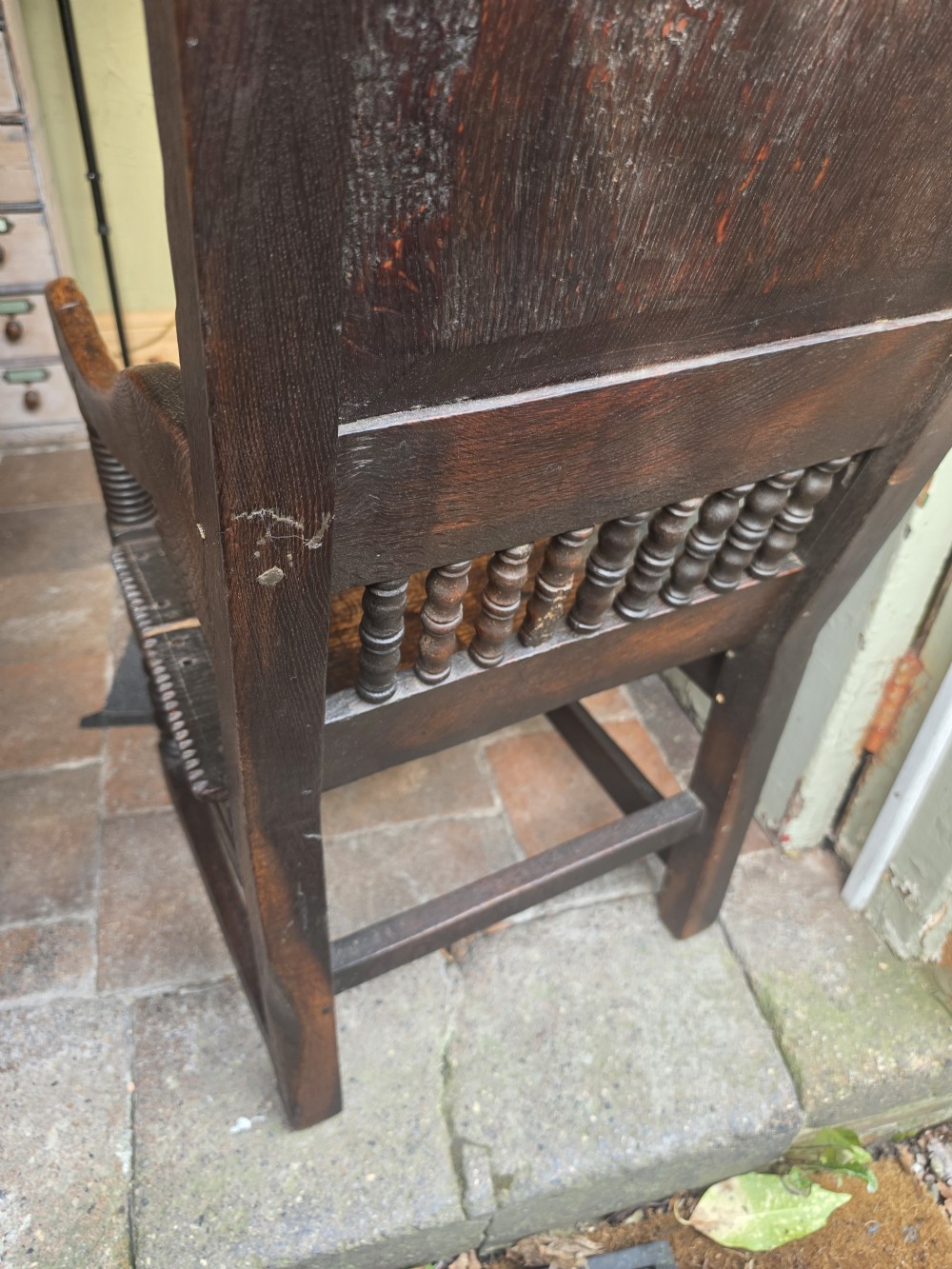 A 17th-century dark oak wainscot armchair featuring a carved back panel with floral inlay, turned front legs, scrolled cresting, and wooden peg joinery. View V