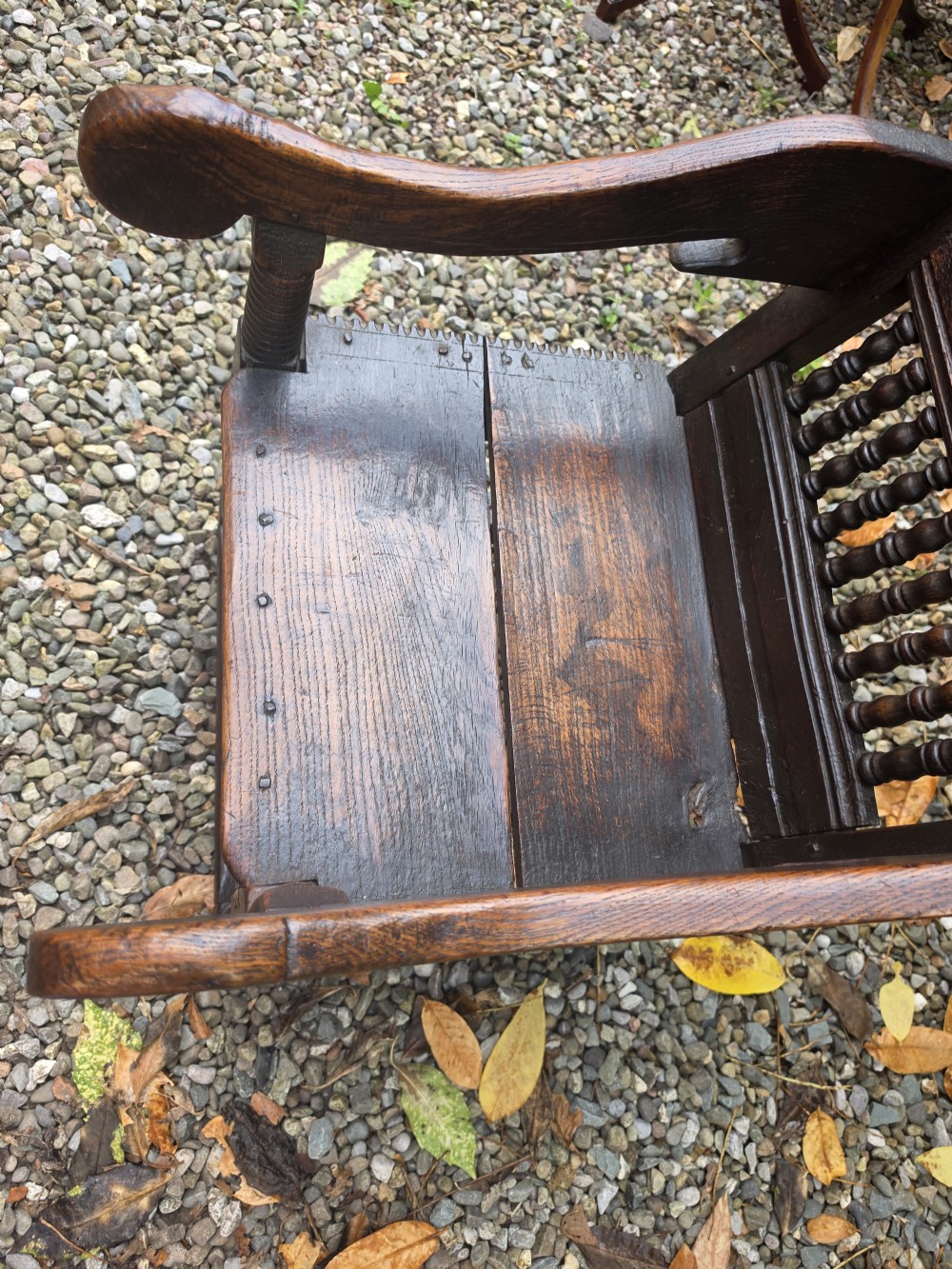 A 17th-century dark oak wainscot armchair featuring a carved back panel with floral inlay, turned front legs, scrolled cresting, and wooden peg joinery. View VII