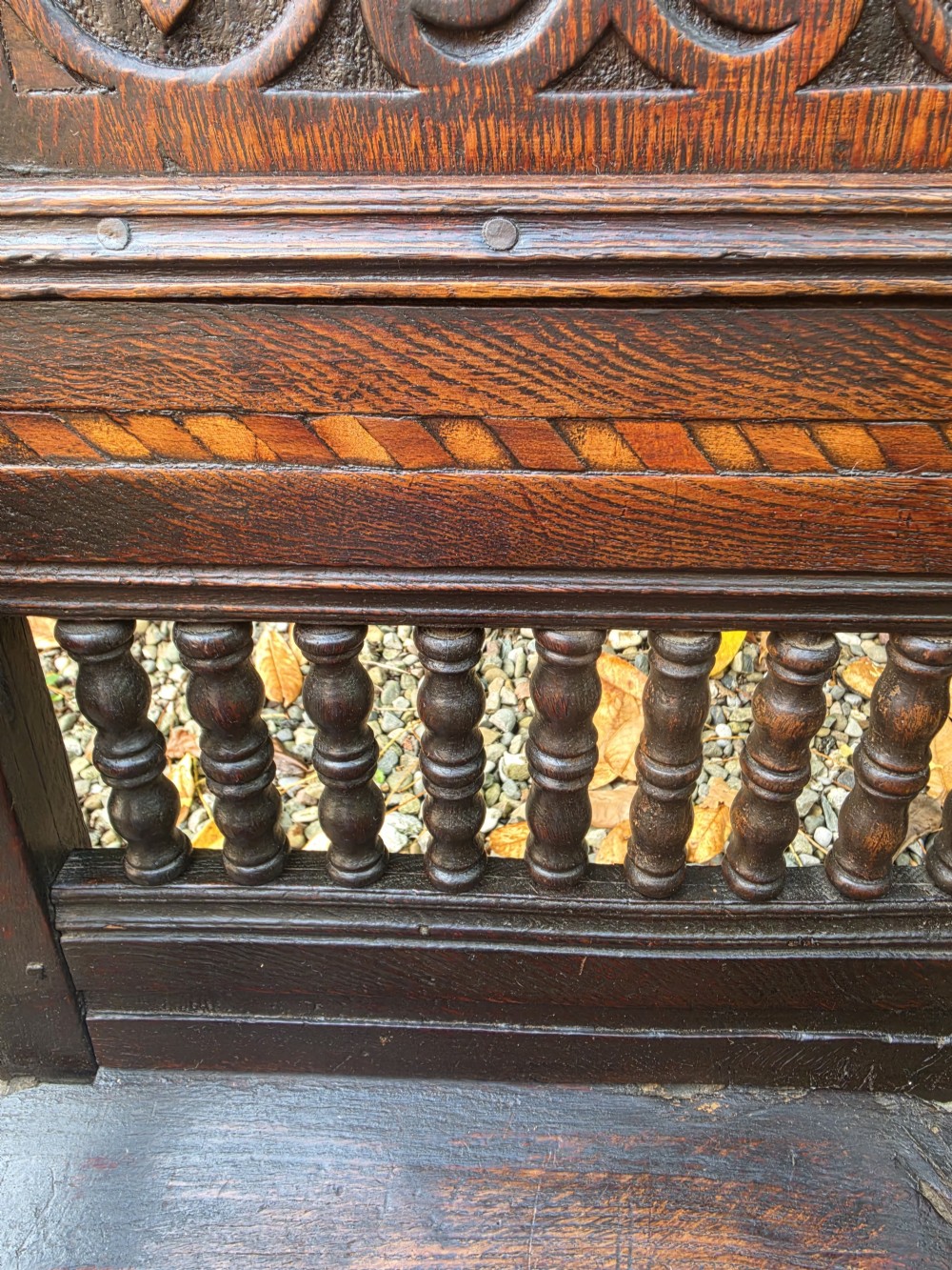 A 17th-century dark oak wainscot armchair featuring a carved back panel with floral inlay, turned front legs, scrolled cresting, and wooden peg joinery. View VIII