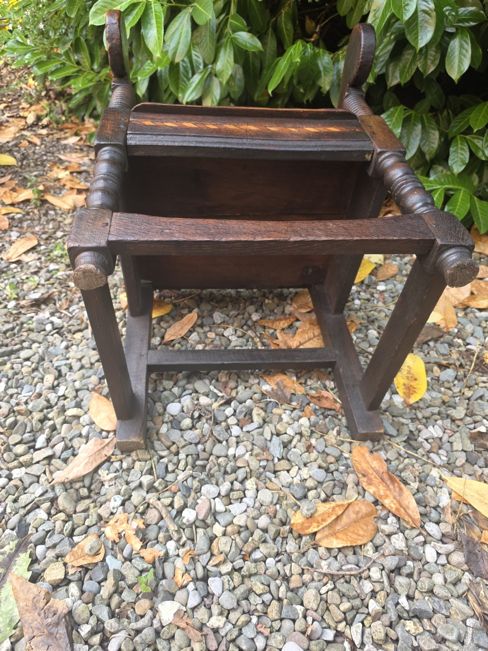 A 17th-century dark oak wainscot armchair featuring a carved back panel with floral inlay, turned front legs, scrolled cresting, and wooden peg joinery. View XI