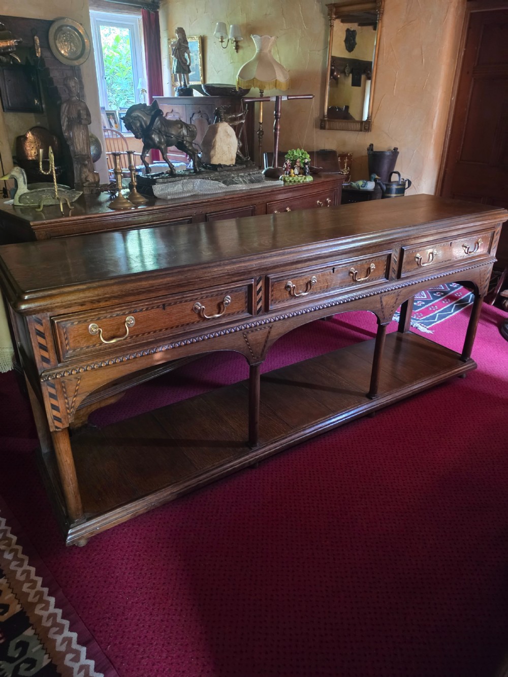 A 19th-century dark oak potboard dresser base featuring three inline drawers with brass swan-neck handles, geometric inlay details, carved arches, and an open lower shelf.