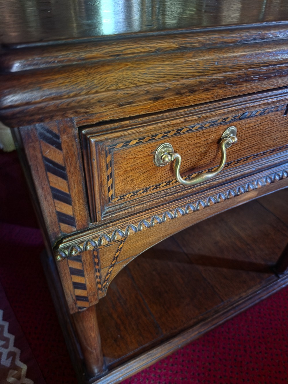 A 19th-century dark oak potboard dresser base featuring three inline drawers with brass swan-neck handles, geometric inlay details, carved arches, and an open lower shelf. View II