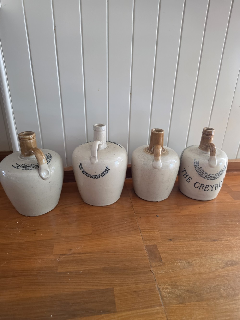 A set of four 19th-century cream stoneware advertising whisky flasks featuring black transfer-printed text and brown glazed spouts. View IV