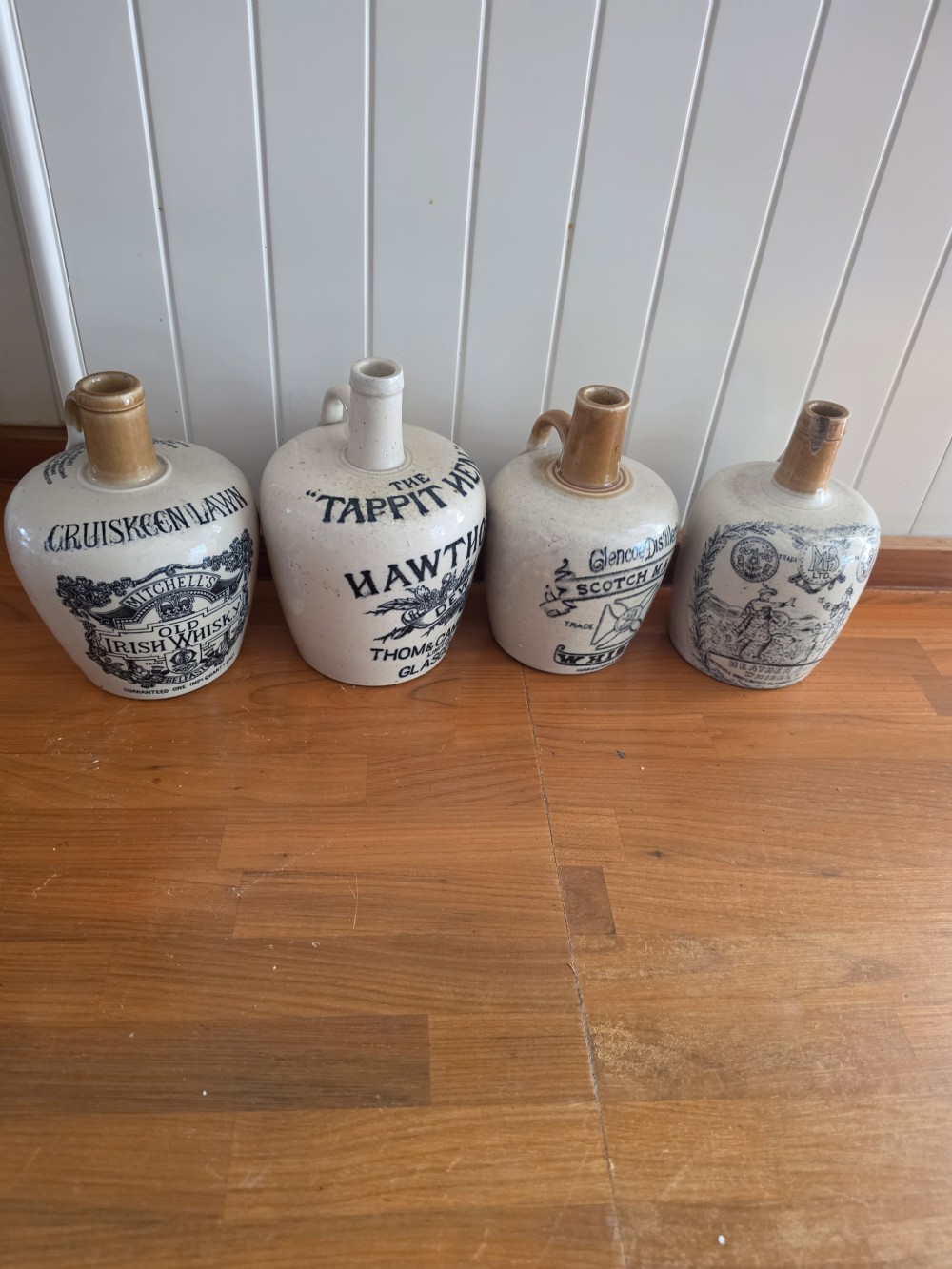 A set of four 19th-century cream stoneware advertising whisky flasks featuring black transfer-printed text and brown glazed spouts. View VI