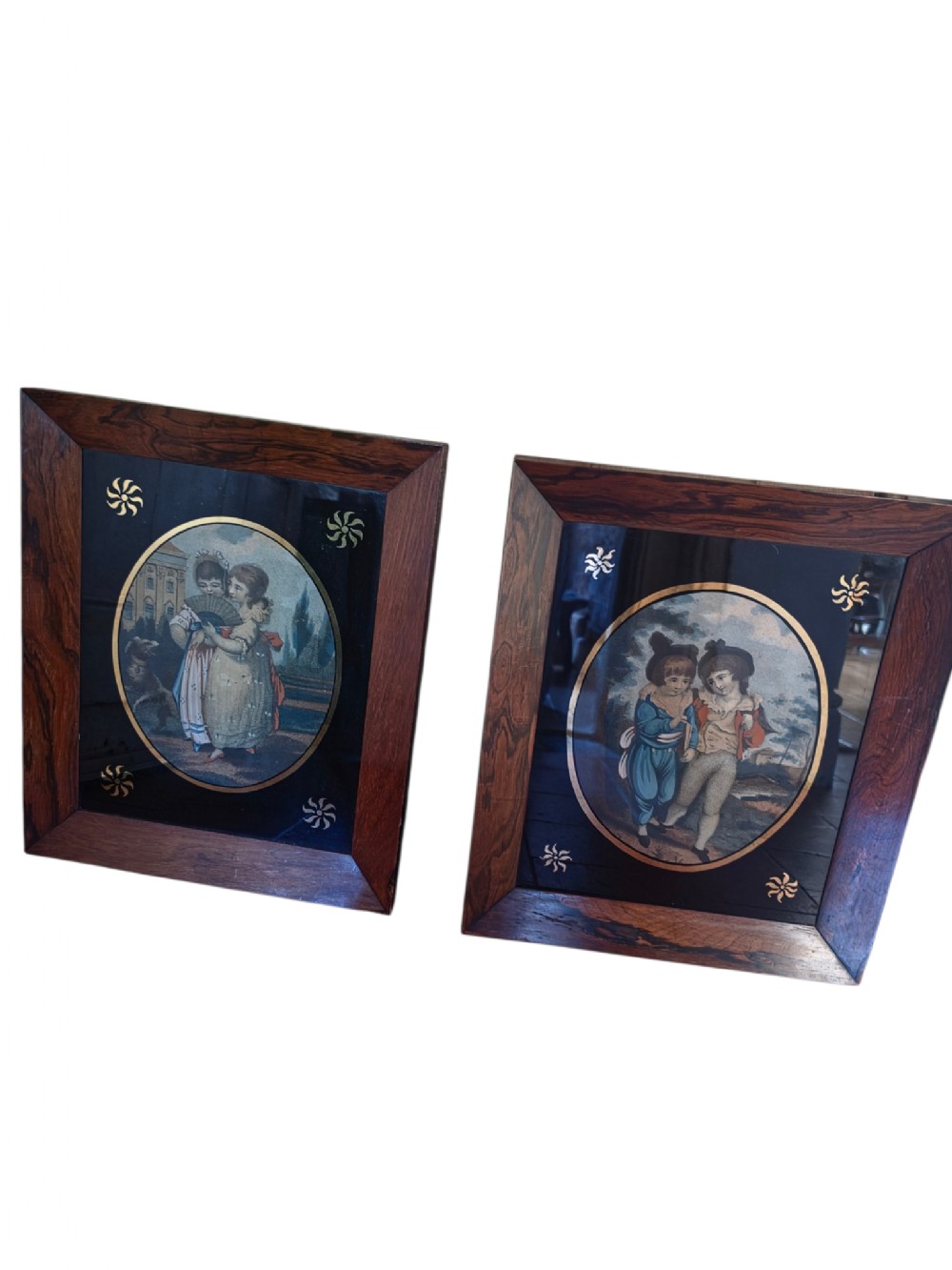 A pair of square rosewood picture frames featuring oval 19th-century prints of children set within black reverse-painted glass mounts with gold motifs.