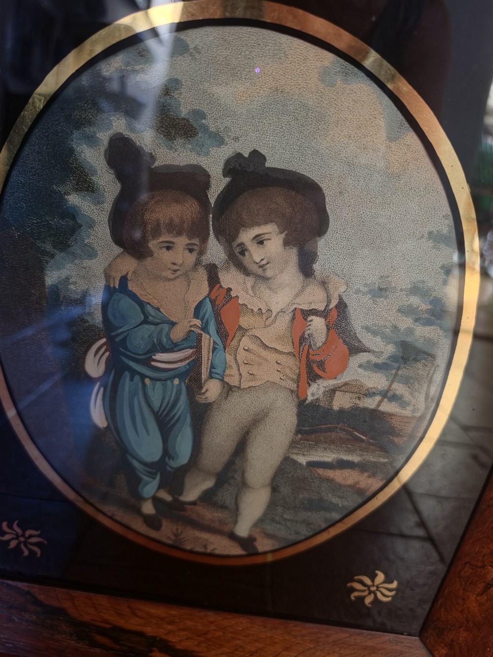 A pair of square rosewood picture frames featuring oval 19th-century prints of children set within black reverse-painted glass mounts with gold motifs. View IV