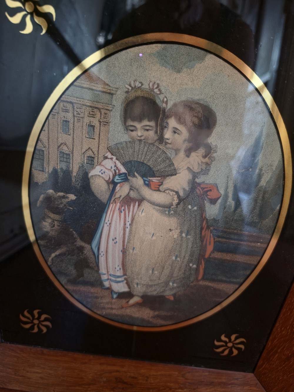 A pair of square rosewood picture frames featuring oval 19th-century prints of children set within black reverse-painted glass mounts with gold motifs. View V